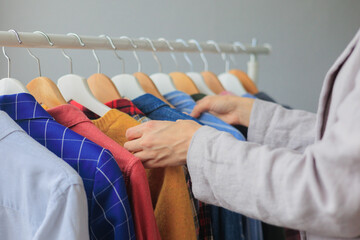 women's hands sort through clothes in wardrobe on hangers, shopping and selection of look for work and meetings. female stylist helps to buy clothes. recycling of textiles, cluttering of the closet at
