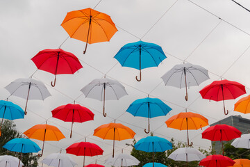 Colorful umbrellas hanging against gray overcast sky and swaying in wind at summer city festival - low angle view. Street decoration, celebration, art, holiday concept