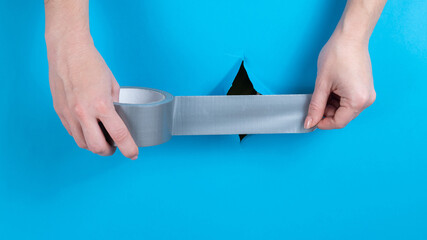 Woman sticking silver tape on a hole on a blue background. 