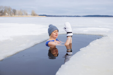 Winter swimming. Woman in frozen lake ice hole. Swimmers wellness and endorphin booster swim in...