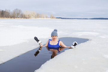 Fototapeta na wymiar Winter swimming. Woman in frozen lake ice hole. Swimmers wellness and endorphin booster swim in cold water. Beautiful female body tempering Cold winter morning landscape. Biohacking routine