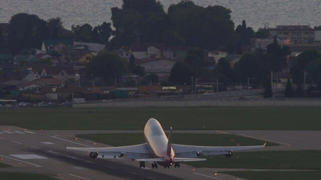 Huge four-engine passenger plane takeoff, sunset pink sky. Jumbo jet departure, rear view. Passenger flight. Flight over the sea