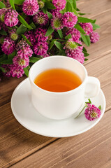 Healthy herbal tea with clover in a white cup on a brown wooden background with a bouquet of clover