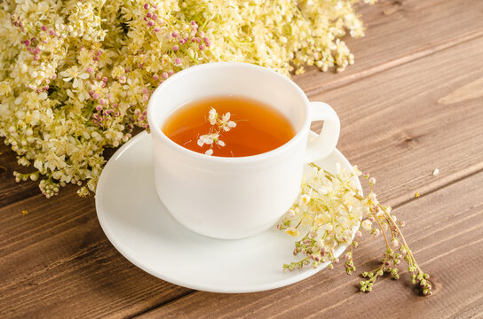 Healthy herbal tea with meadowsweet in a white cup on a brown wooden background with a bouquet of meadowsweet