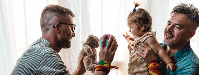 Male gay couple with adopted baby girl at home - Two handsome fathers playing with their daughter -...