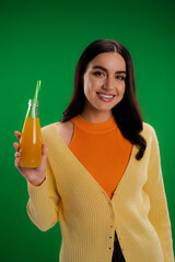 happy brunette woman holding bottle of fresh juice with straw isolated on green.