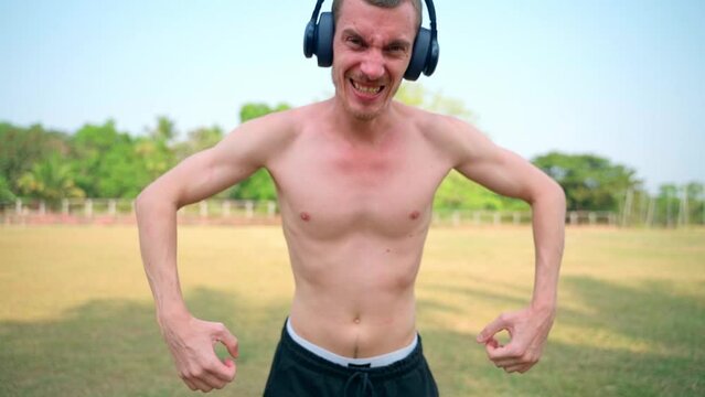 The skinny guy is screaming at the camera, headphones on his head.