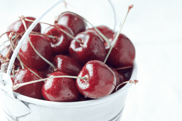 Small white bucket full of red cherries against a light background. Close-up. Bright sunlight.