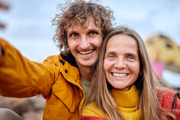 excited couple take photo on smartphone smiling, enjoying time together in nature, caucasian man and woman travel, make selfie on mobile phone, sitting on top of mountains. active lifestyle. close-up
