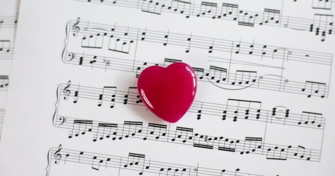 Toy red heart lying on musical notes on paper closeup 4k movie slow motion 