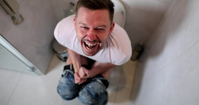 Young man sitting on toilet and screaming in pain during bowel movements 4k movie slow motion 