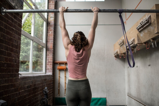 Young woman exercising in gym, hanging from bar