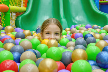 Fototapeta na wymiar A happy girl is having fun playing with colorful balls in the game center