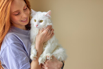 Pets Care. redhead caucasian woman in casual wear holding cat in hands hugging, at home. Friendship.Love. adorable owner with natural red hair with cute purebred white cat. portrait