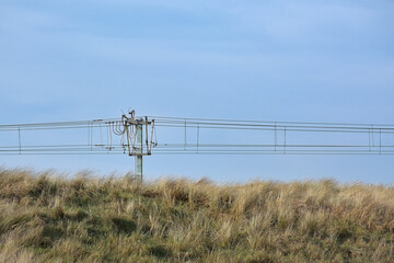 Pylon and wires of the coastal tram infrastructure towering above dune grass on the Belgian coast
