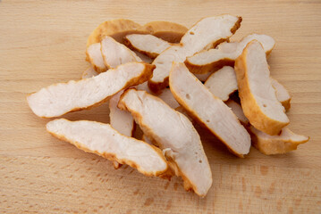 Roasted chicken breast slices on wooden cutting board