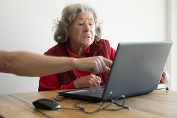 Elderly lady getting help with laptop and internet by a male younger person