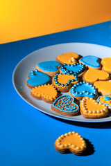 Cookies in shape of hearts decorated by yellow and blue icing and sprinkles on blue plate on blue table against yellow background