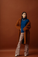 Fashionable confident woman wearing trendy blue turtleneck, brown faux fur coat, chunky chain,...