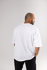 Back view of a bald african american guy with a beard in a white blank t-shirt. Mock-up.