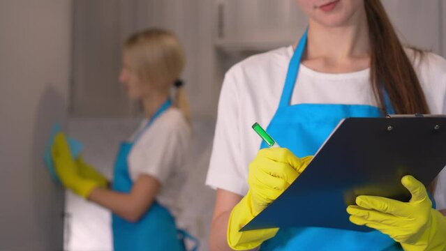 a young cleaner with tablet checks all work performed. Group Dry cleaning company workers in uniform, girl holds tablet device with pen, high quality service. Professional wipers in aprons. Uniform.