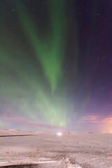 imagen nocturna de un paisaje nevado con una aurora boreal iluminando el cielo de color verde y las estrellas de fondo