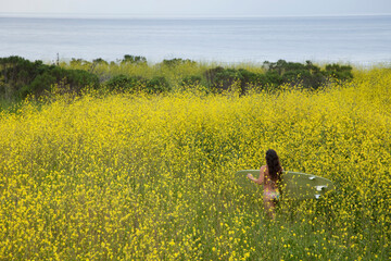 Young woman with her hands outstretched walking to the beach through a field of yellow flowers.
