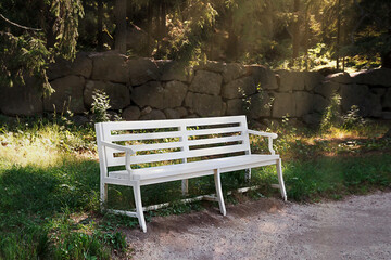 A white bench in the park near a stone fence.