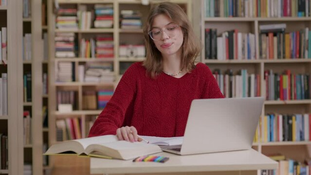 Young woman in library researching with laptop and books 