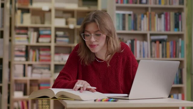 Young female student researching in library using laptop