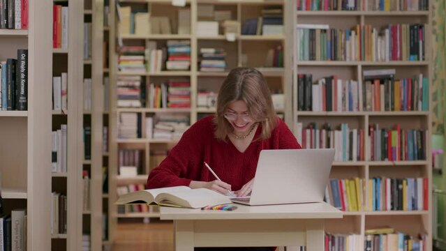 Happy young woman smiling in the library studying using laptop 