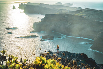Young woman enjoys panoramic view from a steep cliff over the seascape and along the rugged...