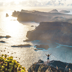 Young woman enjoys panoramic view from a steep cliff over the seascape and along the rugged...