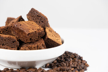 Chocolate cake sliced into squares in a white plate, brownie and coffee beans, copy space for text