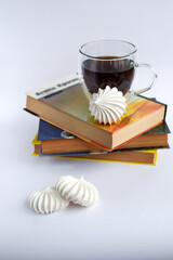 Black tea in an elegant glass cup with white meringue cookies on a stack of books