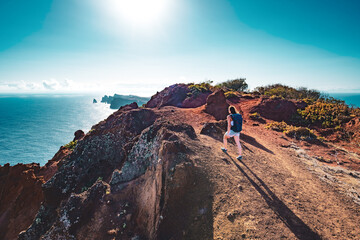 Backpacker woman enjoys hike along a steep cliff overlooking the sea and the rugged foothills of...