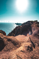 Backpacker woman enjoys hike along a steep cliff overlooking the sea and the rugged foothills of...