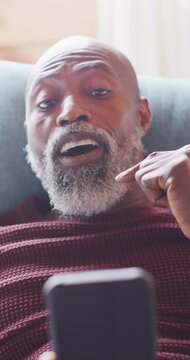 Vertical video of senior african american man spending time in log cabin using smartphone