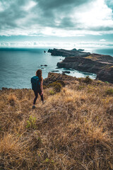 Fototapeta premium Backpacker woman enjoys hike along a steep cliff overlooking the sea and the rugged foothills of Madeira's coast in the morning. Ponta do Bode, Madeira Island, Portugal, Europe.