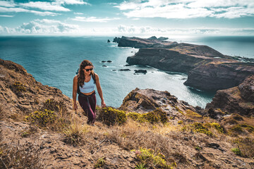 Backpacker woman enjoys hike along a steep cliff overlooking the sea and the rugged foothills of...