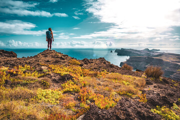 Backpacker woman enjoys panoramic view from a steep cliff overlooking the sea and the rugged...