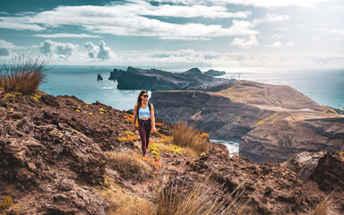 Backpacker woman enjoys hike along a steep cliff overlooking the sea and the rugged foothills of...