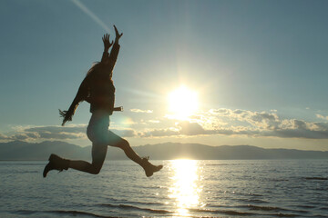 Cheerful woman jumping by lake against sky