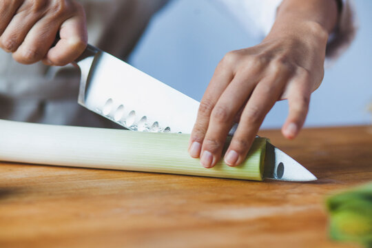 Midsection of woman cutting scallions in kitchen