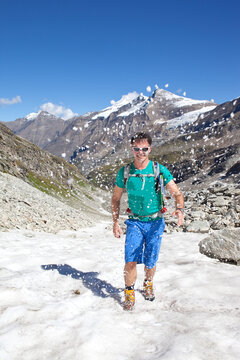 A Male Hiker Walking On Snow In A T-shirt, During The Glocknerrunde, A 7 Stage Trekking From Kaprun To Kals Around The Grossglockner, The Highest Mountain Of Austria.