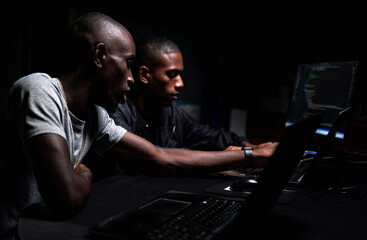 Two black males coding together in a dark room