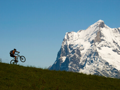 A mountain biker is balancing his bike on slope near Kleine Scheidegg, above Grindelwald. In the background the Scheidegg Wetterhorn mountain.