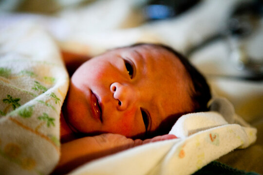 A newborn baby boy lays in bed while midwives preform their newborn screens.