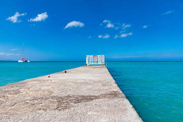 Montego Bay, Steg und Anlegestelle am Strand Doctor’s Cave Beach auf der karibischen Insel Jamaika. Im Hintergrund ein Catamaran und ein blauer Himmel.