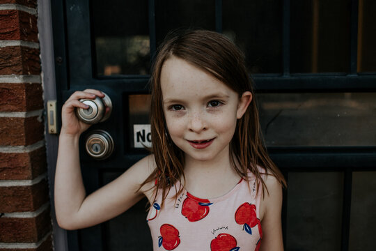 Happy young girl standing outside front door smirking